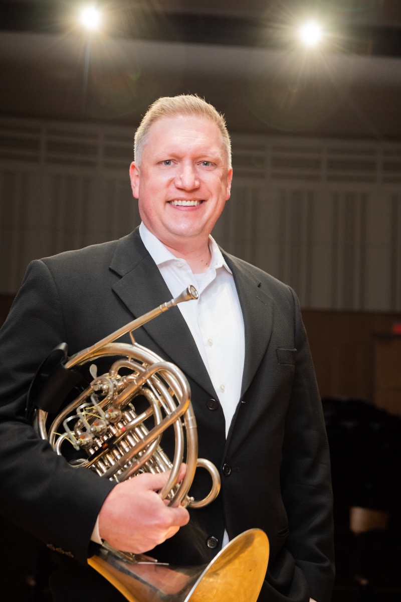 Jason M. Johnston holding his horn on the Hampton School stage